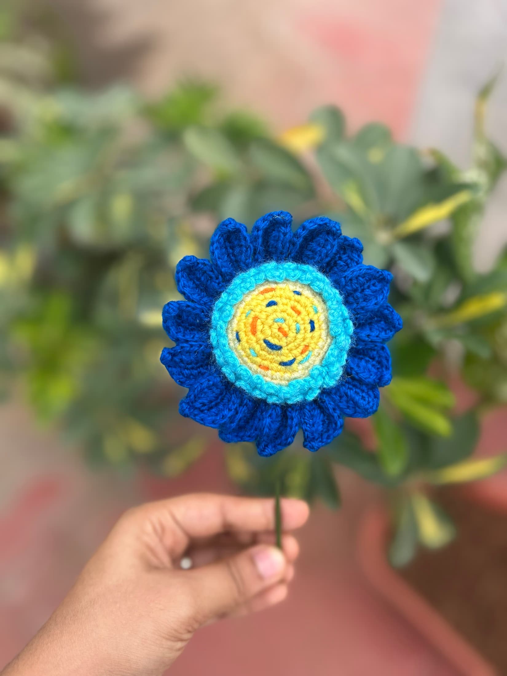 Blue crochet flower held in front of plants